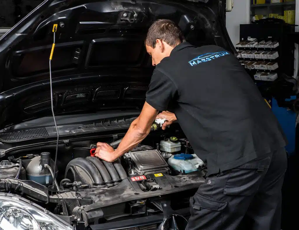 Mecánico con uniforme Maestrum trabajando en el vano motor de un coche